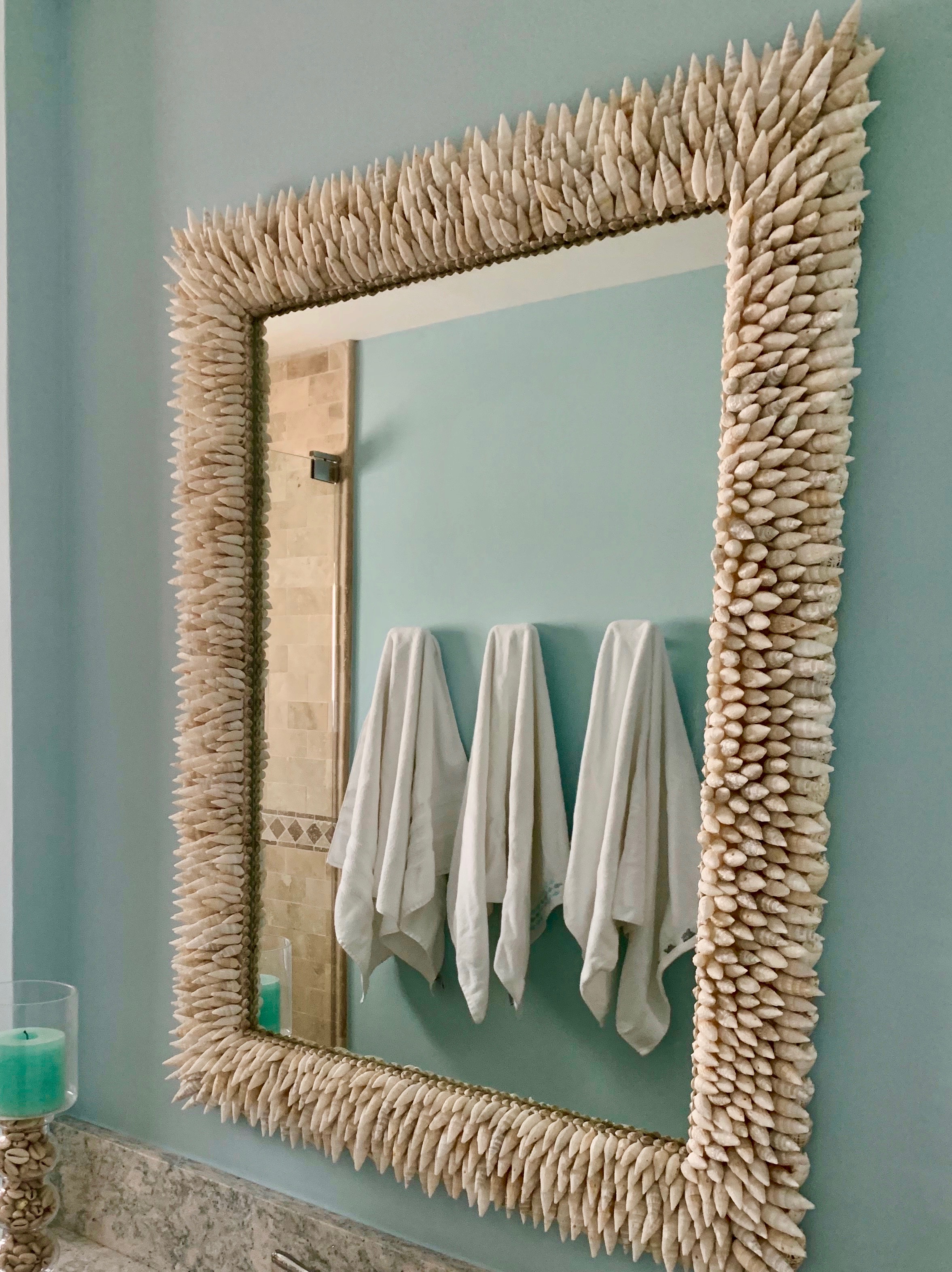 Three bath towels reflected in a mirror made with pointy seashells on a blue wall.