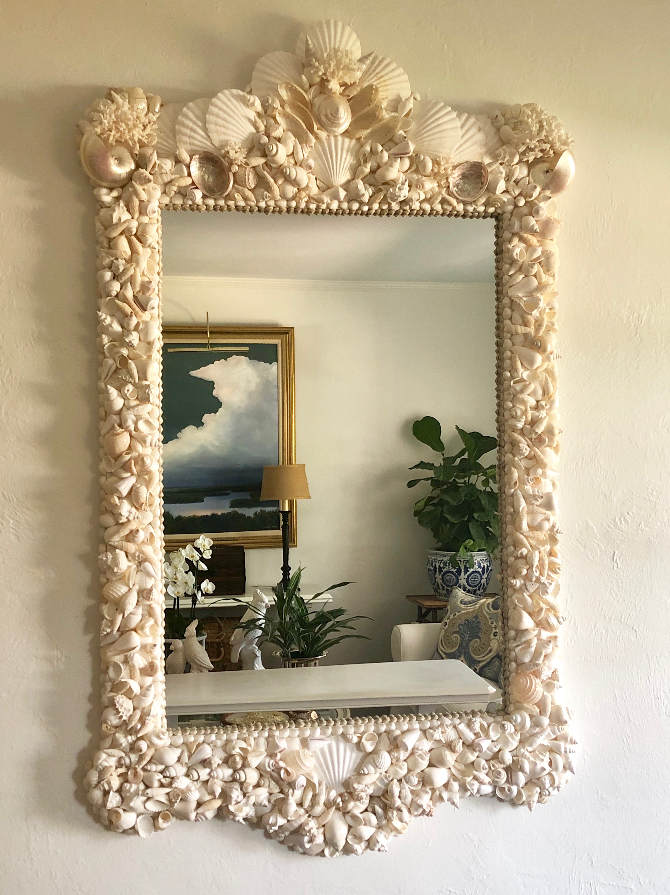 large mirror made with white sea shells reflecting a painting with a large white cloud.