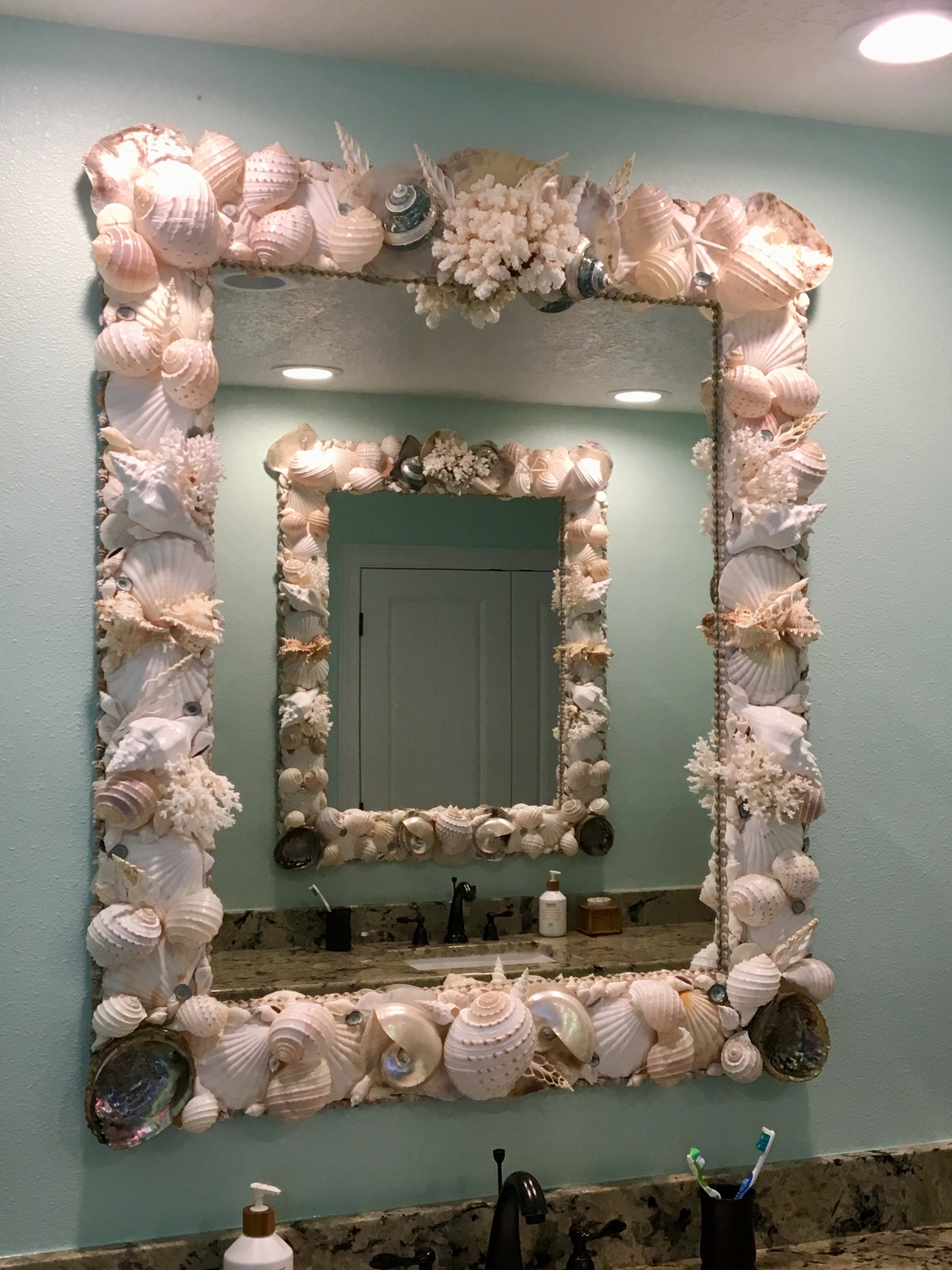 A pair of white and blue mirrors made from shell reflecting each other in a blue bathroom.