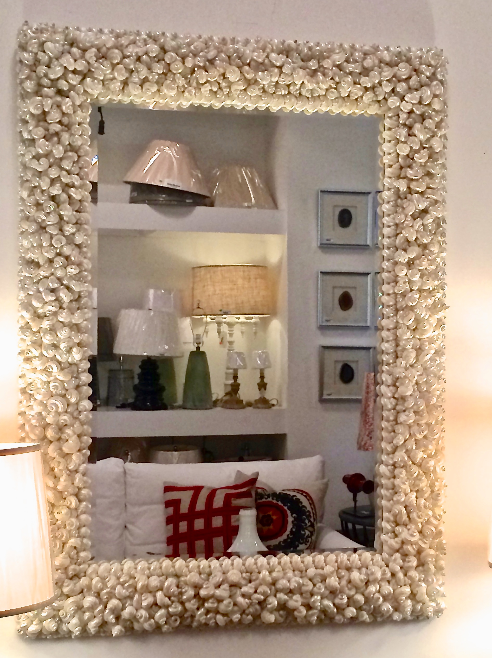 Reflections of a white sofa and lamps for sale in a furniture shop in a mirror made with white seashells.
